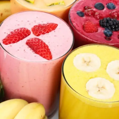 Glasses of strawberry, berry and banana smoothies topped with fresh fruit