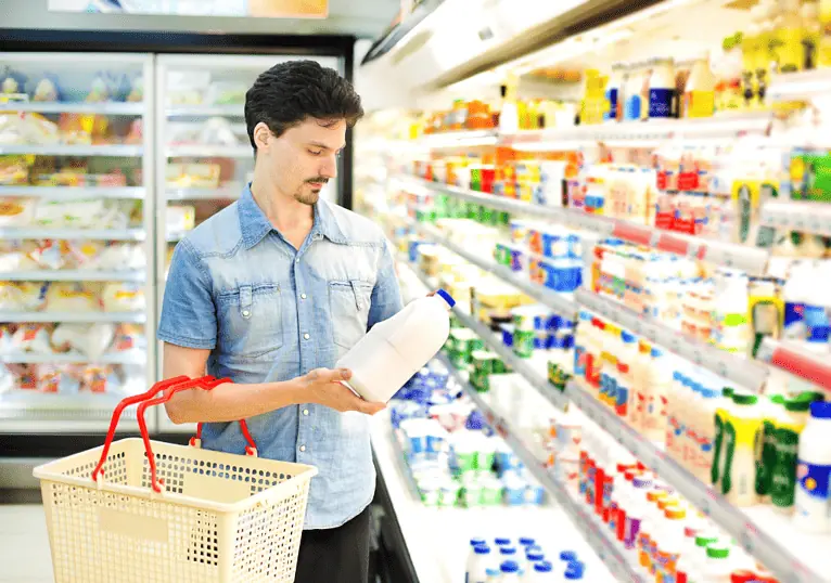 Man in a supermarket dairy aisle reading the label on a bottle of milk
