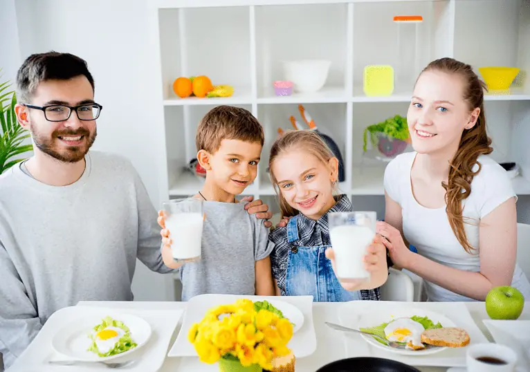 Family at the breakfast table, two children holding up glasses of milk