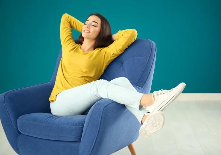 Woman leaning back in a blue armchair with her eyes closed, taking a break