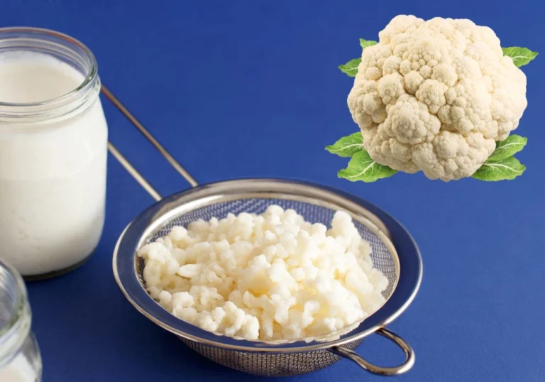 Milk kefir grains in a strainer beside a jar of milk, with a cauliflower to compare their shape